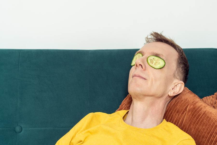 Un homme mettant deux tranches de concombres fines sur ses yeux pour les soulager