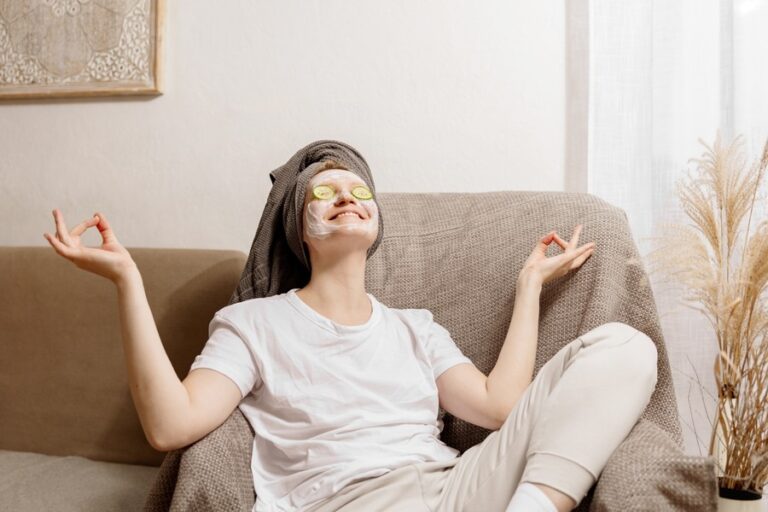 Une femme en position de yoga assise sur un canapé tout en mettant deux tranches fines de concombres pour relaxer ses yeux
