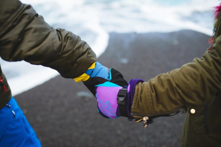 Des mains glissées dans des gants épais, serrés aux poignets, face à un paysage enneigé de montagne