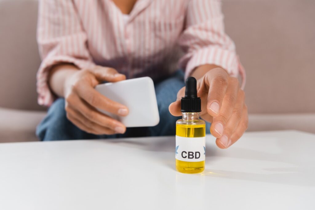Une personne qui tient un téléphone et prend le flacon d'huile de CBD