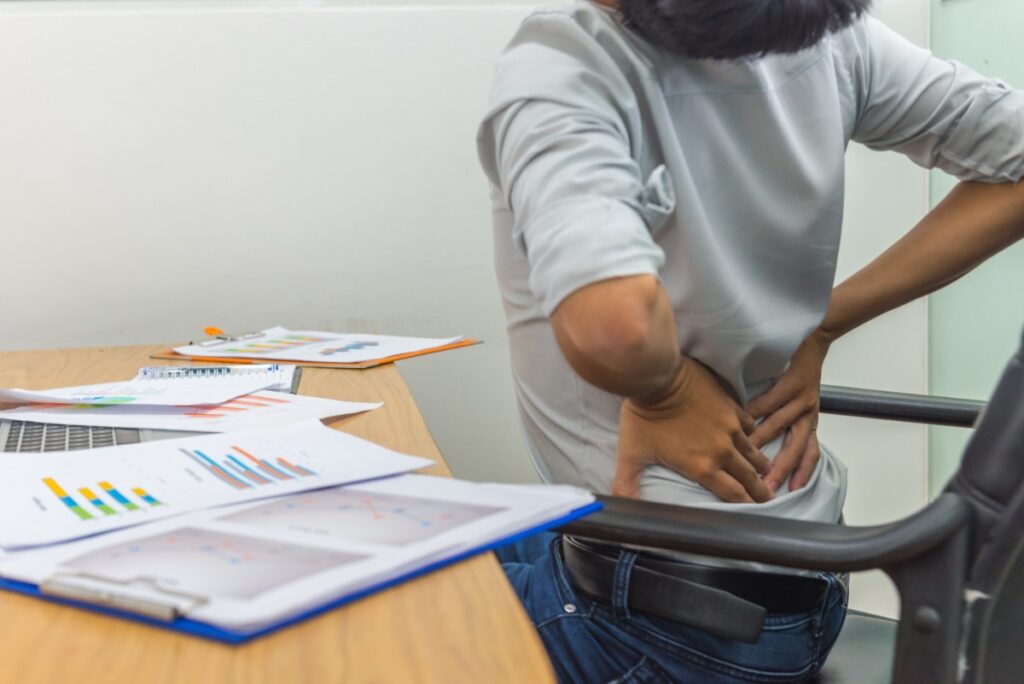 Une femme assise dans son bureau et tient sa hanche