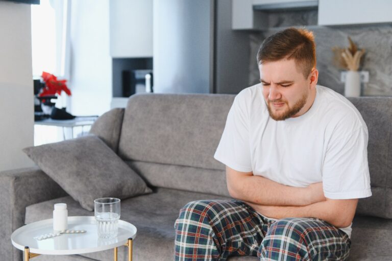 Un homme qui est assis sur un canapé et qui serre son ventre