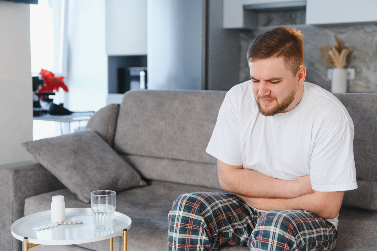 Un homme qui est assis sur un canapé et qui serre son ventre