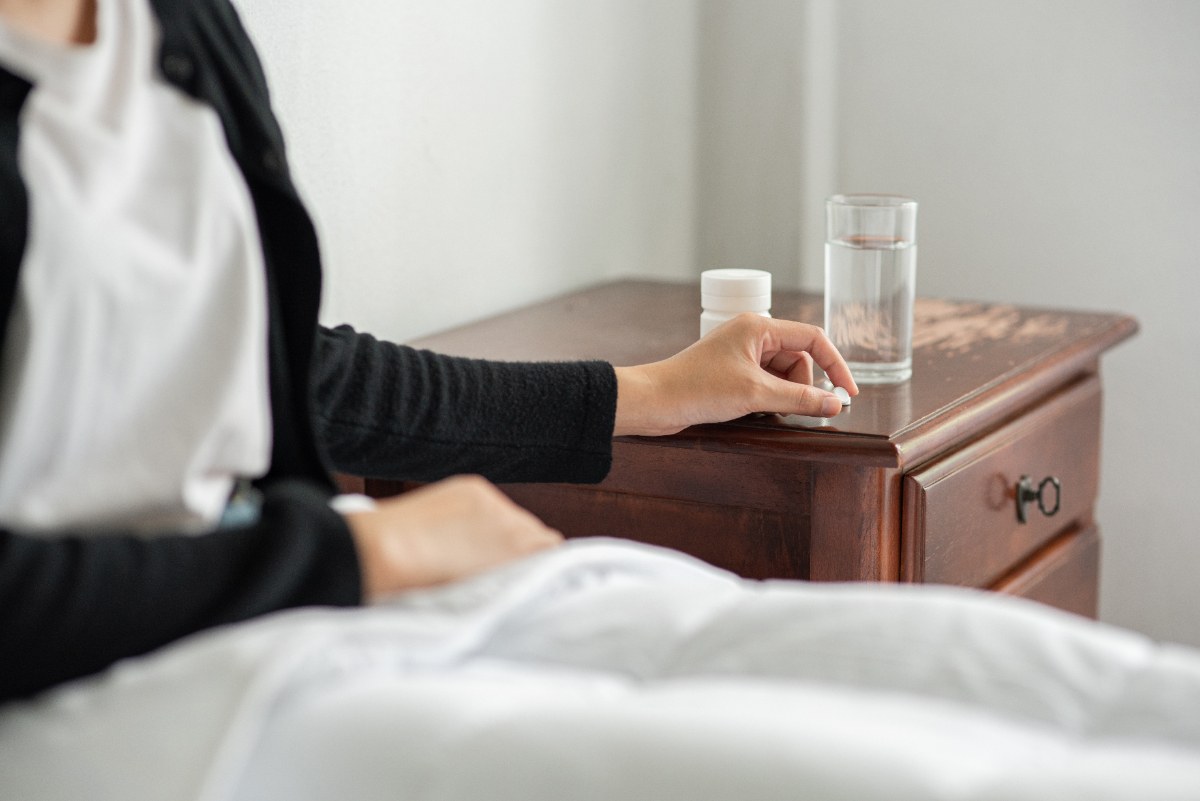Une femme qui prend ses médicaments avec de l'eau sur la table de nuit