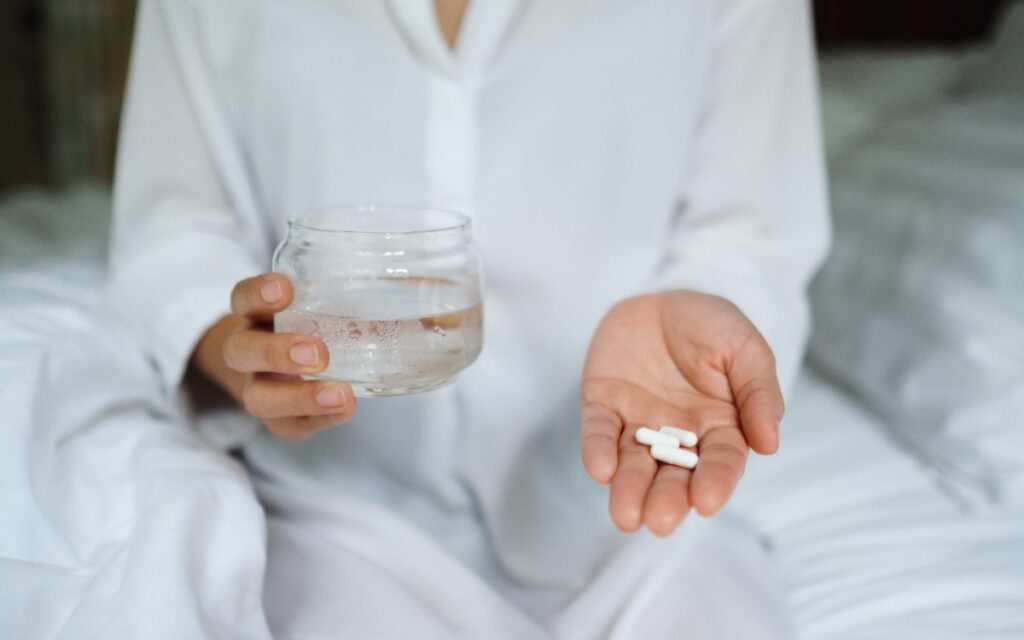 Une femme qui tient de l'eau et des pilules dans sa chambre