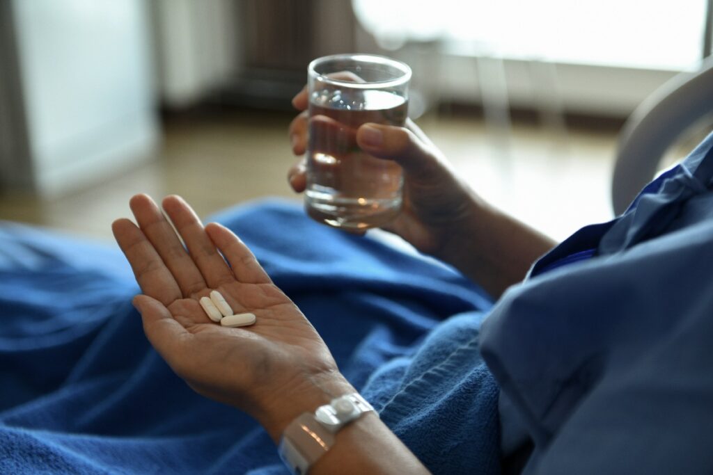 Une personne allongée sur le lit en tenant des pilules et un verre d'eau